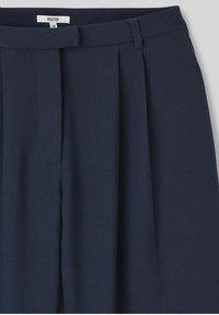 Pantalons plissés bleu marine en tissu lisse, avec une taille et des poches latérales. Le design met en avant une silhouette ajustée.