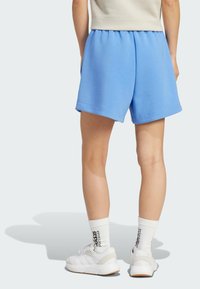 Světle modré bavlněné šortky s elastickým pasem, které mají volný střih, ohrnuté lemy a jsou kombinovány s bílými teniskami a ponožkami.