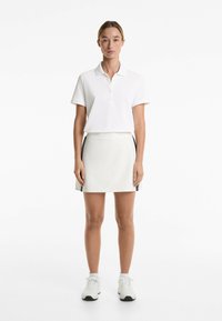 White polo shirt with short sleeves and button placket, paired with a white skirt featuring side stripes. Shoes are white athletic sneakers.