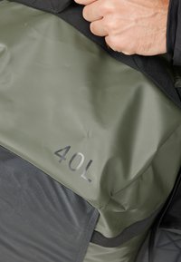 Kantokassi med 40L kapasitet, laget av grønt vannavstøtende materiale med teksturert overflate og sorte detaljer; har et solid grep.