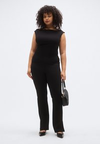 Mustast kapuutsiga parajalt istuv t-särk, mida on kombineeritud mustade lõhestatud pükstega. Aksessuaaridena on väike must käekott ja madalad mustad kingad.