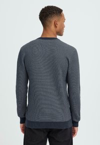 Tengerészkék kötött pulóver hosszú ujjakkal, bordás mandzsettával és aljjal, texturált mintával és klasszikus kerek nyakkivágással, hátulról nézve.