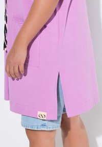 Paarse tuniek met een zijnaad en een voorzak, gemaakt van lichtgewicht stof. Gecombineerd met denimshorts en voorzien van een merketiket.