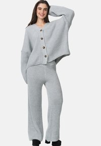 Pullover grigio chiaro a costine con scollatura a V e grandi bottoni dorati, abbinato a pantaloni a costine coordinati, caratterizzati da una vestibilità comoda e gambe larghe.
