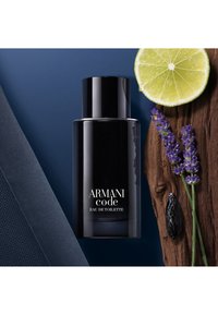 Flacon noir d'Armani Code Eau de Toilette à côté d'une moitié de citron, de brins de lavande et d'un tissu sombre texturé sur une surface bleue.