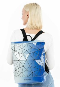 Mėlyna geometrinė kuprinė su blizgiu paviršiumi, pasižyminti triaukštėmis juodomis kontūro formomis. Į komplektą įeina reguliuojamos juodos petnešos ir užtrauktukas.