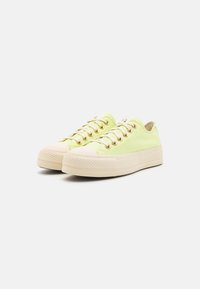 Limettengrüne Leinen-Sneaker mit goldenen Ösen, runder beigefarbener Zehenkappe und strukturiertem Gummi-Sohle; mit Schnürdesign.