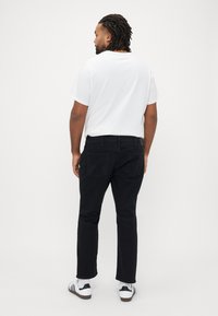 Μαύρο τζιν παντελόνι σε ίσια γραμμή, με πίσω τσέπες και απλό σχέδιο, συνδυασμένο με λευκό T-shirt και λευκά αθλητικά παπούτσια.