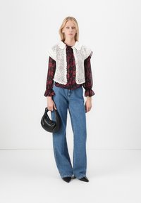 Gilet bianco di maglia sopra una blusa floreale scura, abbinato a jeans blu a vita alta. Completato con una borsa nera e tacchi a punta.