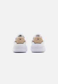 Weiße Sneaker mit einem glatten Obermaterial aus Synthetik, beigen Wildlederakzenten an der Ferse und geprägtem Logo auf der Ferse. Dicke weiße Gummisohle.