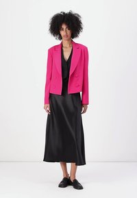 Blazer roz intens G cu două rânduri de nasturi, purtat peste o rochie neagră satinat cu bretele, având un decolteu în V și lungime până la glezne, asociat cu pantofi negri.