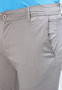 Jasnoszare spodnie z prostym przodem, detalem guzikowym w talii i bocznymi kieszeniami o gładkiej bawełnianej fakturze.