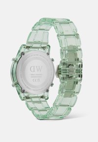 Reloj transparente verde con una pulsera de acrílico gruesa y una caja redonda. Cuenta con una parte trasera de acero inoxidable y eslabones rectangulares claros.