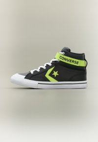 Μαύρο ψηλό αθλητικό παπούτσι Converse με λευκά κορδόνια, λογότυπο με αστέρι σε νέον πράσινο και λουράκι στον αστράγαλο σε νέον πράσινο με την ένδειξη "CONVERSE" σε ουδέτερο φόντο.