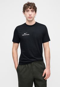 Crna pamučna majica kratkih rukava s bijelim Nike logom i tekstom "NIKE OFFICIAL" na prsima. Ima okrugli izrez i klasičan kroj.