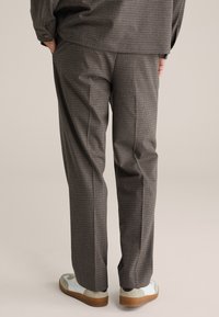 Brązowe spodnie w kratę o luźnym kroju, z gładką fakturą i wyraźnymi kantami, zestawione z casualowymi białymi i szarymi trampkami.