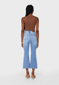 Bruine mouwloze top gecombineerd met lichtblauwe wijde jeans met een hoge taille en rafelige zoom, gedragen met naakte open teen hakken.