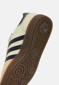 Crèmekleurige sneaker met zwarte strepen, een gestructureerde rubberen zool en een zacht bovenmateriaal. Voorzien van een ronde neus en vetersluiting.