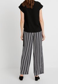 Svart kort top som matchar med högmidjade, vida byxor som har djärva svartvita vertikala ränder. Slät tygtextur.