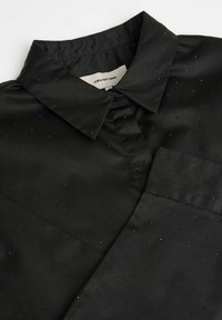 Czarna satynowa koszula z kołnierzykiem, zdobiona teksturowanym wzorem małych, błyszczących kropek oraz kieszenią na lewej piersi.