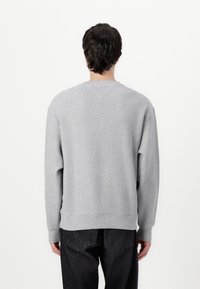 Grey sweatshirt with a textured finish, crew neck, and ribbed cuffs. Shown from the back, paired with dark jeans.