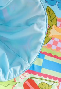 Tissu bleu clair au toucher doux, présentant un motif floral avec des couleurs vives sur un fond coloré et texturé.