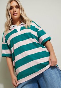 Grön och rosa randig pikétröja med vit krage, korta ärmar och avslappnad passform; tyget ser mjukt och avslappnat ut, med sidslitsar.