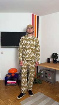 Σύνολο σε πράσινο και λευκό σχέδιο με πουκάμισο με κουμπιά και παντελόνι, κατασκευασμένο από υφασμάτινη ύφανση. Μαύρα sneakers συμπληρώνουν το σύνολο.