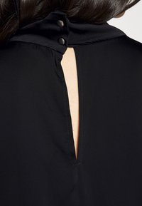 Blusa nera con colletto bottonato con due bottoni in metallo e apertura a occhiello sul retro, realizzata in tessuto morbido.