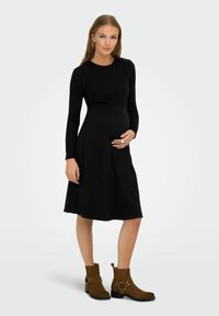 Robe de maternité noire en tricot avec de longues manches côtelées et un corsage ajusté. Assortie à des bottines en suède marron à lacets avec des accents de boucles.
