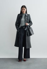 Black leather trench coat, gray turtleneck, high-waisted navy pants, red block-heeled shoes, and a black bag with perforated details.
