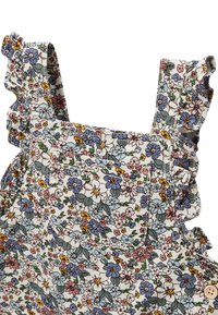 Salopette florale avec des bretelles à volants. Présente un fond blanc avec des fleurs colorées en rose, bleu et jaune. Comprend une poche.