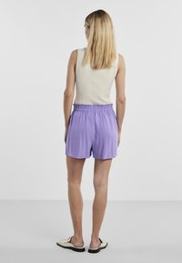 Shorts violet clair avec une ceinture élastique, fabriqués en tissu doux. Stylisés avec un débardeur crème côtelé, vus de dos.