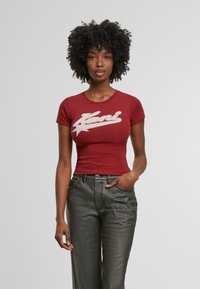 Bordeaux rood t-shirt met korte mouwen en een wit tekstlogo op de voorkant. Skinny fit, gemaakt van zachte katoen, gecombineerd met donkergrijze jeans.