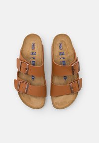 Brown faux leather sandals with two adjustable straps, copper-colored buckles, and a cork footbed featuring blue printed branding.