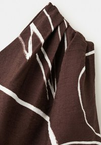 Tissu marron avec des motifs de lignes abstraites blanches rassemblées en haut, montrant la texture et des plis doux sur un fond uni.