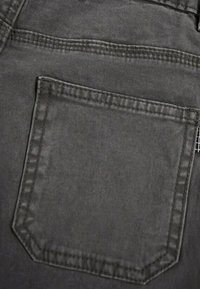 Tessuto di denim grigio con una tasca posteriore rettangolare cucita, caratterizzata da una texture sottile e bordi rinforzati, che mettono in risalto la sua praticità.