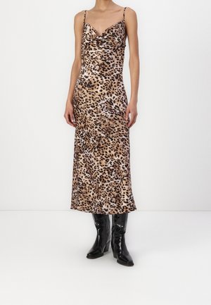 Frau trägt ein ärmelloses Midikleid mit Leopardenmuster, einem Wasserfallausschnitt und schwarzen Lederstiefeln mit Absatz.