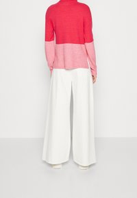 Rot-rosa Farbverlauf Pullover mit strukturiertem Finish, kombiniert mit weißen, weit geschnittenen Hosen. Das Outfit zeichnet sich durch eine lockere Passform und einen lässigen Stil aus.