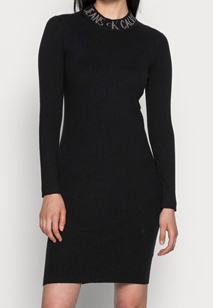 Sort ribbet bodycon-kjole med lange ærmer, tætsiddende silhuet og logo-tekst på den runde halsudskæring.