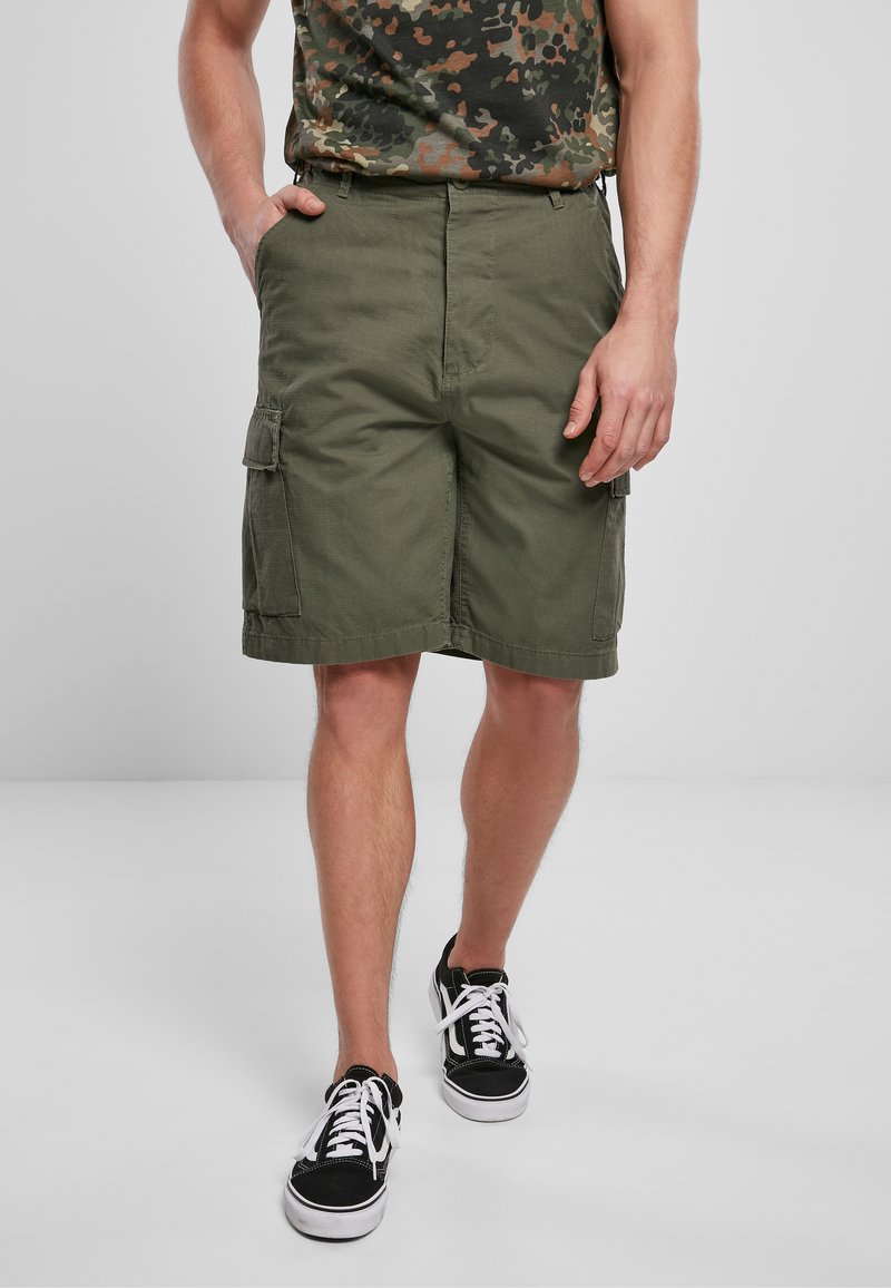 Pantaloni cargo verde oliva caratterizzati da più tasche laterali, una vestibilità comoda e un tessuto in misto cotone. Indossati con sneakers nere.