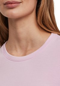 T-shirt rosa chiaro a maniche corte con scollo rotondo, tessuto morbido e dettagli di cucitura discreti attorno al colletto.