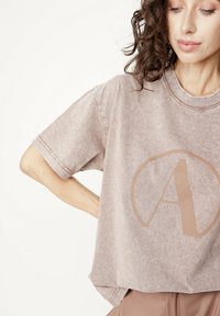 Jasnobrązowy, oversize t-shirt z miękkiej, teksturowanej tkaniny, z dużym taupe nadrukiem litery „A” i okrągłym dekoltem. Krótkie rękawy z obszytymi krawędziami.