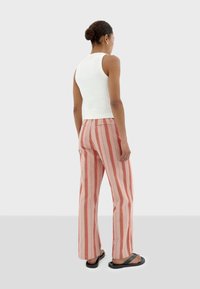 Witte geribde tanktop gecombineerd met roze en witte verticaal gestreepte wijduitlopende broek. Het model staat in zwarte slippers voor een neutrale achtergrond.