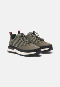 Zapatos de senderismo verdes con material de ante, presentan acentos de malla gris, suela de goma negra y están estilizados con cordones elásticos y lengüetas rojas.