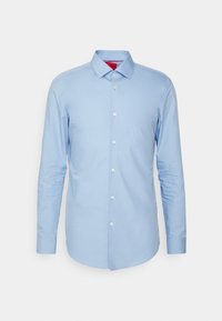 Chemise habillée homme bleu clair à manches longues avec col pointu et boutons blancs sur le devant, sur un fond blanc uni.