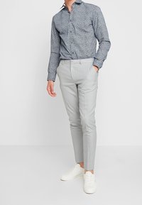 Knappad skjorta i marinblått med vit geometrisk tryck, kombinerad med ljusgrå slim-fit byxor och vita sneakers. Slät tygfinish.