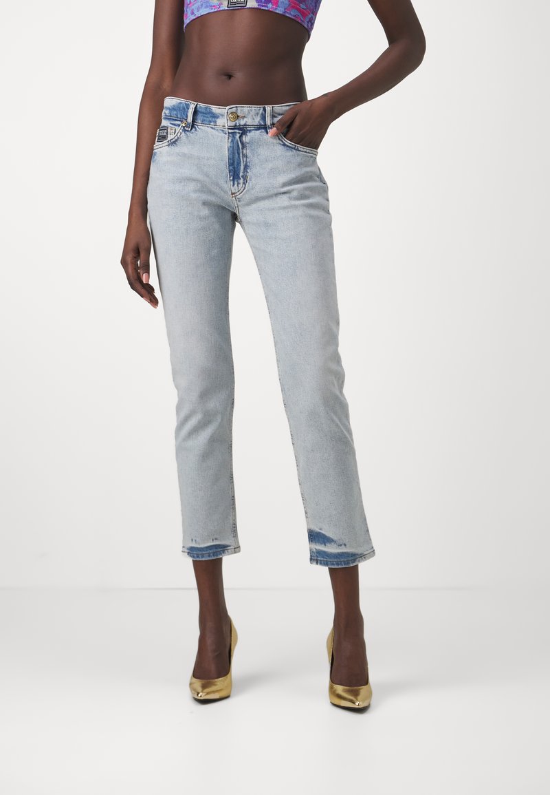 Jasnoniebieskie dżinsy o prostym kroju, z lekkimi przetarciami na końcach, pięcioma kieszeniami i zapięciem na guzik. Noszone z złotymi szpilkami.