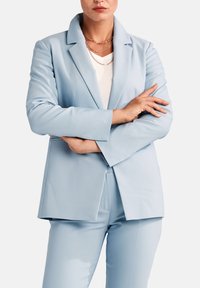 Ljusblå skräddarsydd kavaj i mjukt tyg, med spetsig slag, långa ärmar och rak skärning, i kombination med matchande byxor.