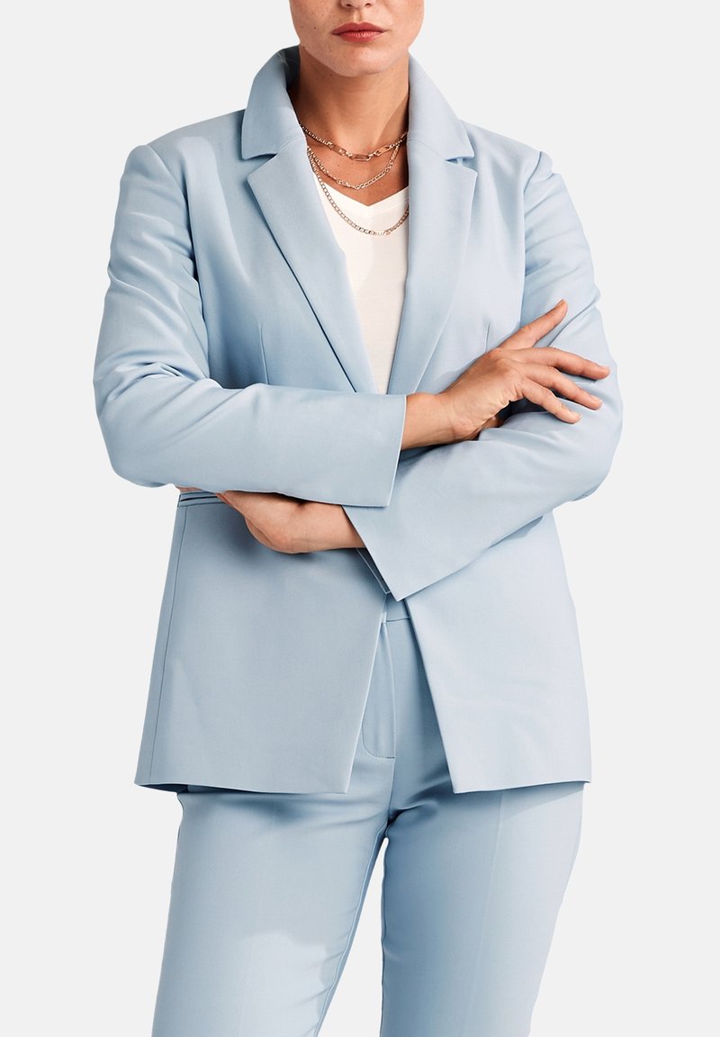 Ljusblå skräddarsydd kavaj i mjukt tyg, med spetsig slag, långa ärmar och rak skärning, i kombination med matchande byxor.